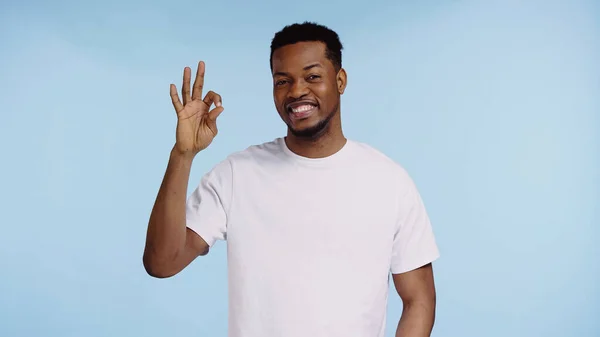 Glücklicher afrikanisch-amerikanischer Mann in weißem T-Shirt mit Okay-Zeichen isoliert auf blau — Stockfoto