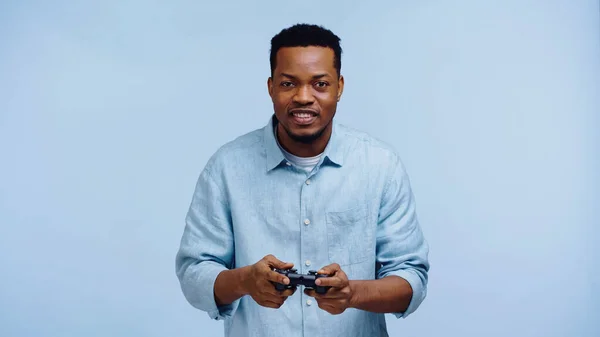 КИЕВ, УКРАИНА - 22 НОЯБРЯ 2019 года: счастливый африканский американец, играющий в видеоигру изолированный на синем — стоковое фото