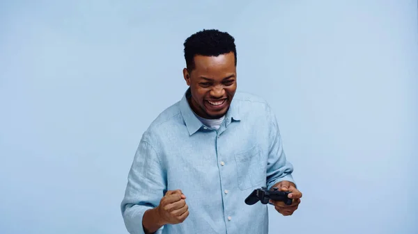 KIEW, UKRAINE - 22. NOVEMBER 2019: glücklicher afrikanisch-amerikanischer Mann hält Steuerknüppel und jubelt isoliert auf blauem Grund — Stockfoto