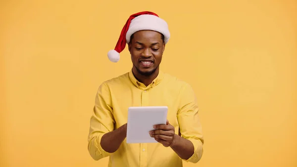 Щасливий афроамериканський чоловік у капелюсі Санта використовує цифровий планшет ізольований на жовтому — стокове фото