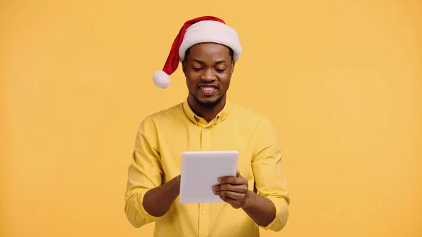 Heureux homme afro-américain chapeau santa en utilisant une tablette numérique isolé sur jaune — Photo de stock