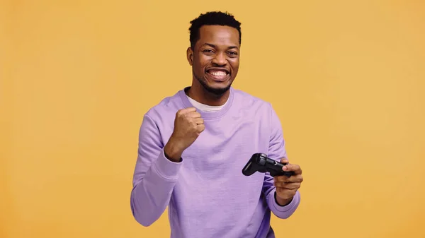 KYIV, UKRAINE - NOVEMBER 22, 2019: happy african american man holding joystick and rejoicing isolated on yellow — Stock Photo