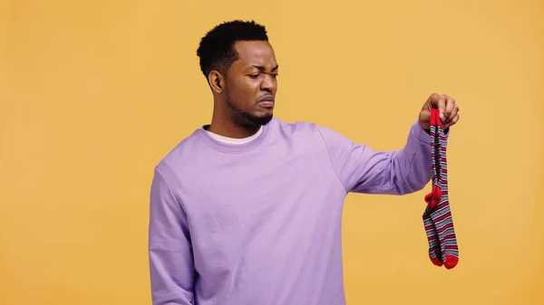 African american man holding stinky socks isolated on yellow — Stock Photo