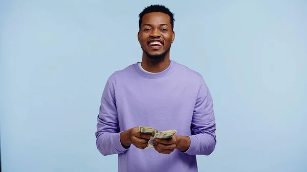 Hombre afroamericano feliz contando billetes de dólar aislados en azul - foto de stock