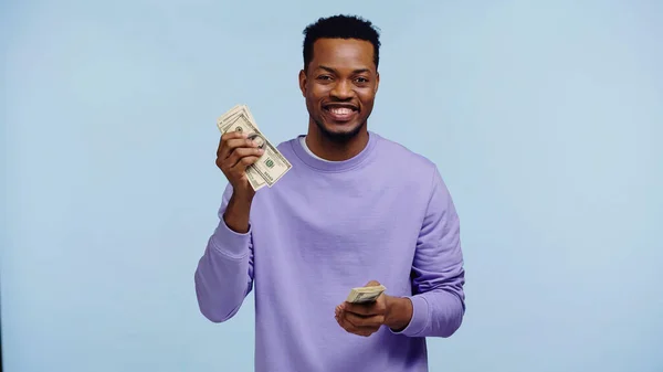 Happy african american man holding money isolated on blue — Stock Photo