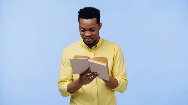 Hombre afroamericano inteligente en camisa amarilla libro de lectura aislado en azul - foto de stock