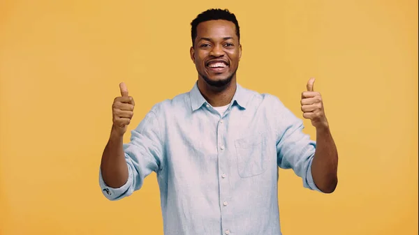 Feliz homem americano africano em camisa azul mostrando polegares para cima isolado no amarelo — Fotografia de Stock