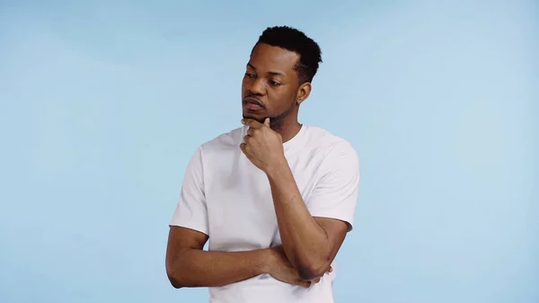 Hombre afroamericano pensativo en camiseta blanca mirando hacia otro lado aislado en azul - foto de stock