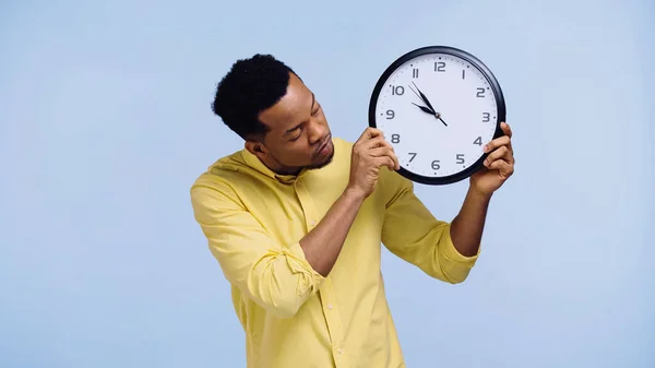 Hombre afroamericano en camisa amarilla sosteniendo reloj aislado en azul - foto de stock