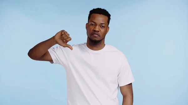 Hombre afroamericano en camiseta mostrando el pulgar hacia abajo aislado en azul - foto de stock