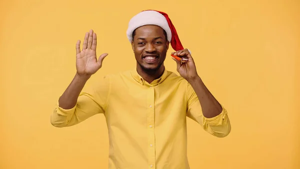 Feliz homem afro-americano em santa chapéu acenando mão isolada em amarelo — Fotografia de Stock