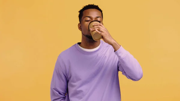 Hombre afroamericano en jersey púrpura bebiendo café para ir aislado en amarillo - foto de stock