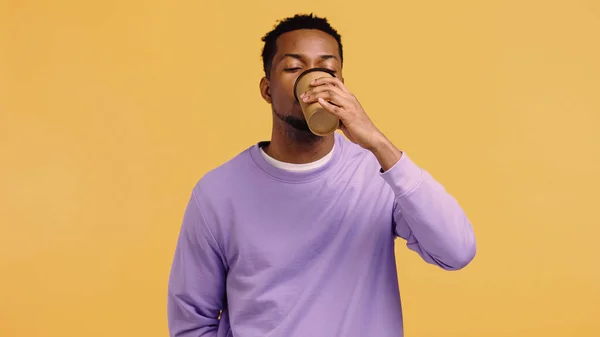 African american man in purple pullover drinking coffee to go isolated on yellow — Stock Photo