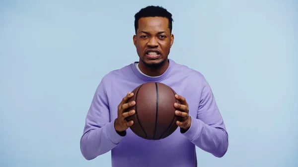 Hombre afroamericano disgustado sosteniendo baloncesto aislado en azul — Stock Photo