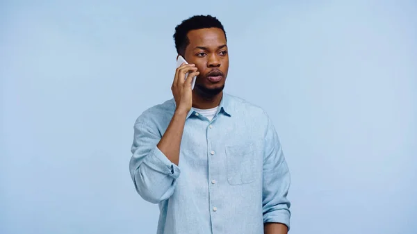 Africano americano hombre en camisa hablando en móvil aislado en azul - foto de stock