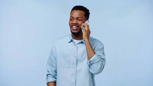 Homem americano africano alegre na camisa que fala no celular isolado no azul — Fotografia de Stock