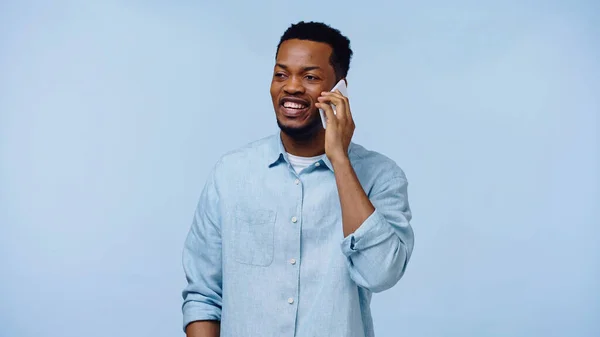 Alegre africano americano hombre en camisa hablando en celular aislado en azul - foto de stock