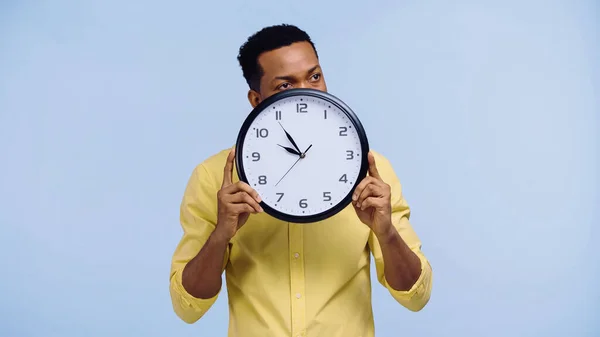 Homme afro-américain tenant horloge et regardant loin isolé sur bleu — Photo de stock