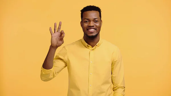Positive african american man in shirt showing ok sign isolated on yellow — Stock Photo
