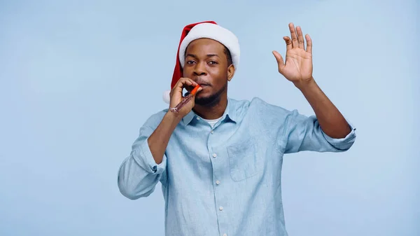 Афроамериканський чоловік у капелюсі Санта дує партійний ріг і жестикулює ізольовано на синьому — стокове фото