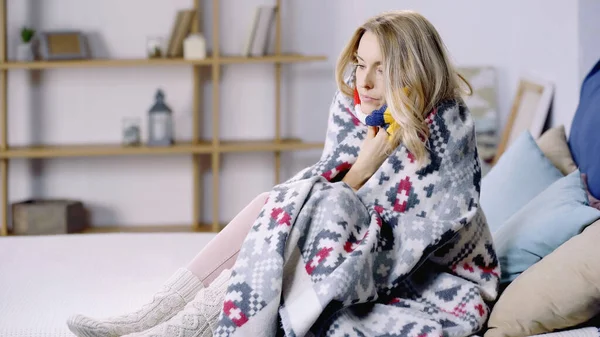 Sick and sad woman sitting on bed under colorful blanket — Stock Photo