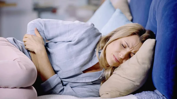 Mujer agotada con los ojos cerrados que sufren de dolor abdominal y acostada en la cama — Stock Photo
