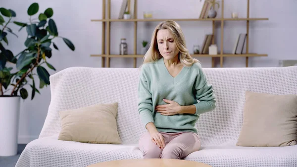 Mujer agotada que sufre de dolor abdominal y se sienta en el sofá — Stock Photo