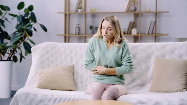 Exhausted woman with closed eyes having cramps while sitting on couch — Stock Photo