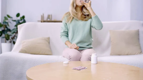 Abgeschnittene Ansicht einer Frau, die Pille nimmt und Wasser im Wohnzimmer trinkt — Stockfoto