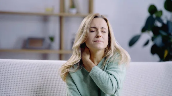 Mujer triste y rubia con los ojos cerrados teniendo dolor en el cuello - foto de stock