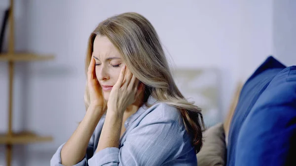 Mujer triste con los ojos cerrados teniendo migraña mientras toca la cabeza en el dormitorio - foto de stock