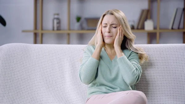 Femme triste avec les yeux fermés ayant migraine tout en touchant la tête dans le salon — Photo de stock