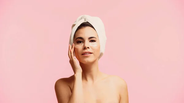 Young woman with bare shoulders applying moisturizing eye patches isolated on pink — Stock Photo