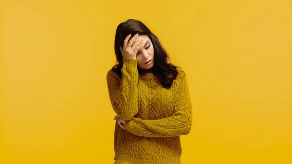 Bouleversée et brune femme en pull touchant le front isolé sur jaune — Photo de stock