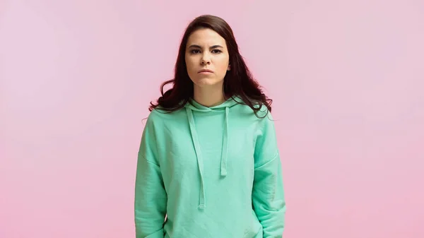 Displeased and brunette woman in turquoise hoodie looking at camera isolated on pink — Stock Photo