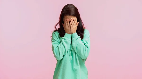 Brünette Frau in türkisfarbenem Kapuzenpulli verdeckt Gesicht, während weint isoliert auf rosa — Stockfoto