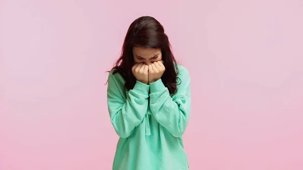 Young brunette woman in turquoise hoodie covering face and crying isolated on pink — Stock Photo