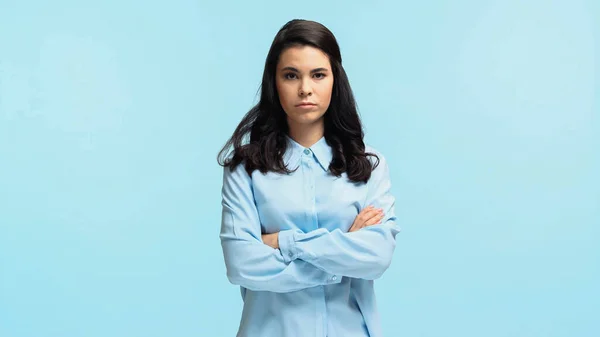 Offended young woman in shirt standing with crossed arms isolated on blue — Stock Photo