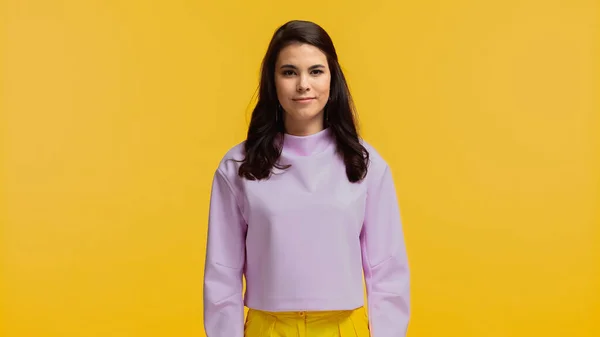 Brunette woman in purple sweatshirt standing and looking at camera isolated on yellow — Stock Photo