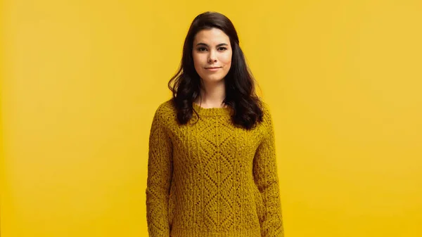 Young and brunette woman in sweater looking at camera isolated on yellow — Stock Photo