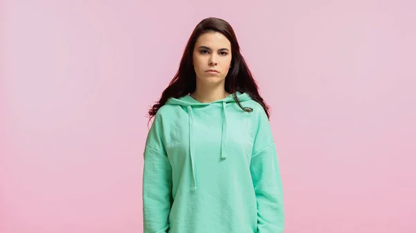 Triste et jeune femme en sweat à capuche turquoise regardant la caméra isolée sur rose — Photo de stock