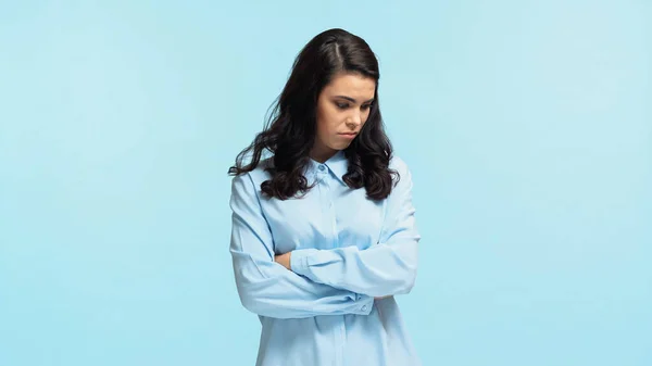 Triste jovem mulher de camisa de pé com os braços cruzados isolado em azul — Fotografia de Stock