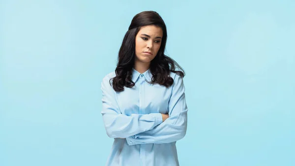 Displeased young woman in shirt standing with crossed arms isolated on blue — Stock Photo