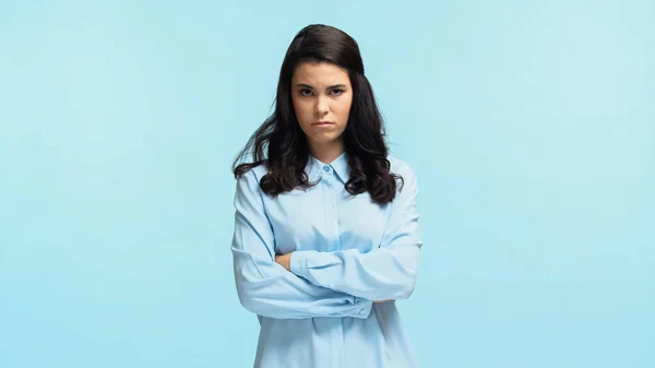 Displeased young woman in shirt standing with crossed arms and looking at camera isolated on blue — Stock Photo