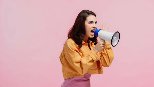 Mulher morena gritando ao fazer anúncio em alto-falante isolado em rosa — Fotografia de Stock