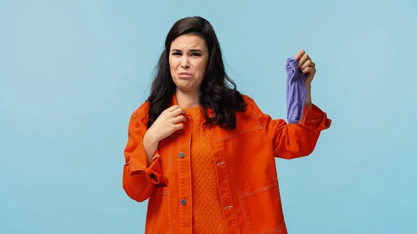 Mujer joven disgustada en chaqueta naranja sosteniendo calcetines apestosos aislados en azul - foto de stock