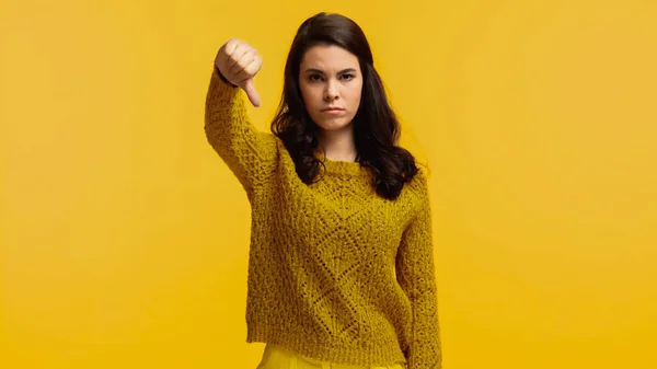 Unzufriedene brünette Frau im Pullover zeigt Daumen nach unten vereinzelt auf gelb — Stockfoto