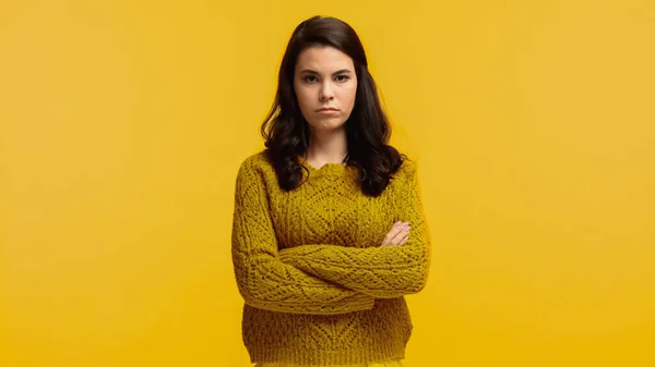 Mulher morena descontente em suéter de pé com braços cruzados isolados no amarelo — Fotografia de Stock