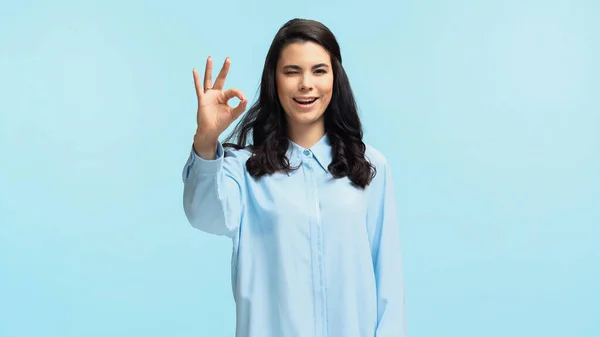 Feliz jovem mulher na camisa olhando para a câmera ao mostrar ok isolado em azul — Fotografia de Stock