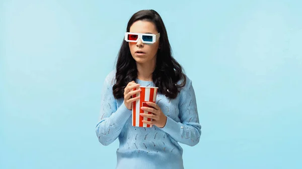 Brünette junge Frau in 3D-Brille hält Popcorn in der Hand und schaut sich Film isoliert auf blau an — Stockfoto